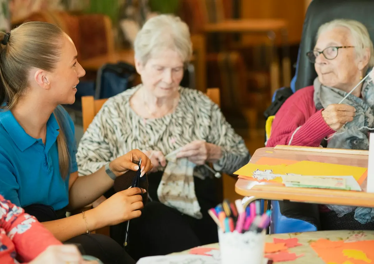 Older women knitting and drawing at a table with a carer