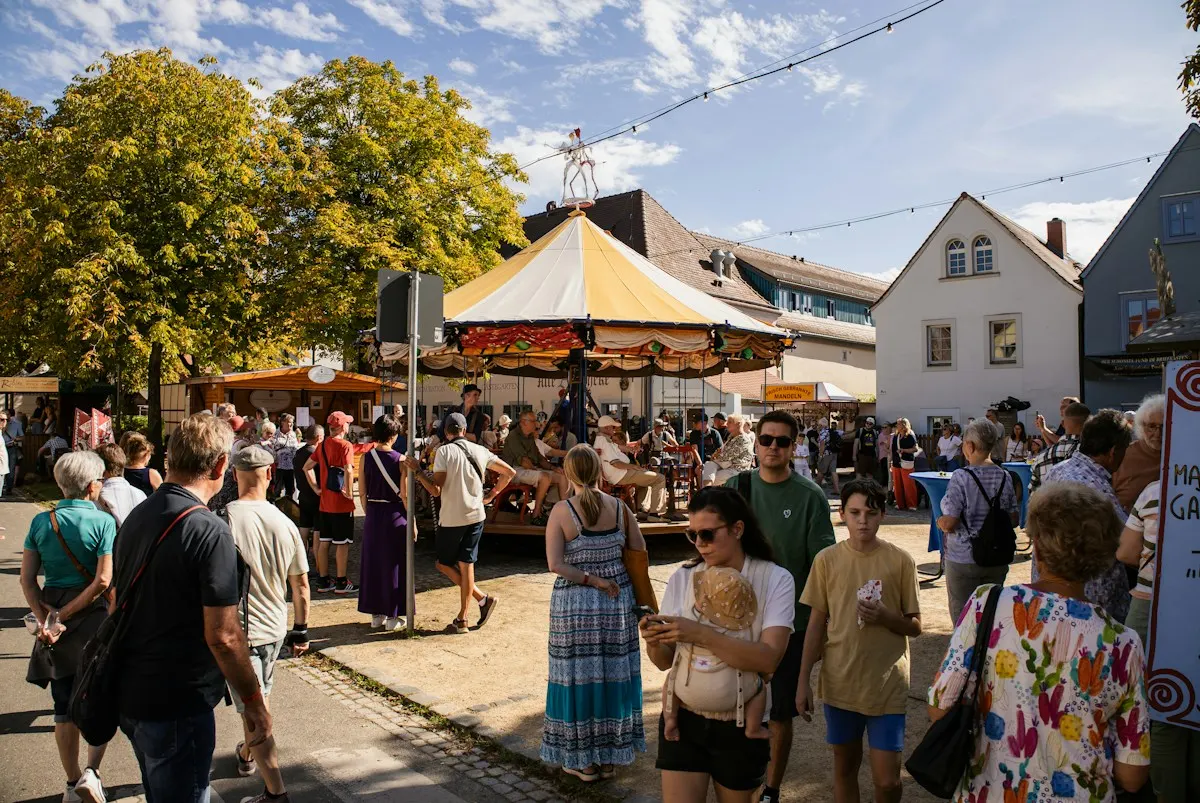 Crowds at an outdoor fair with a carousel and bunting