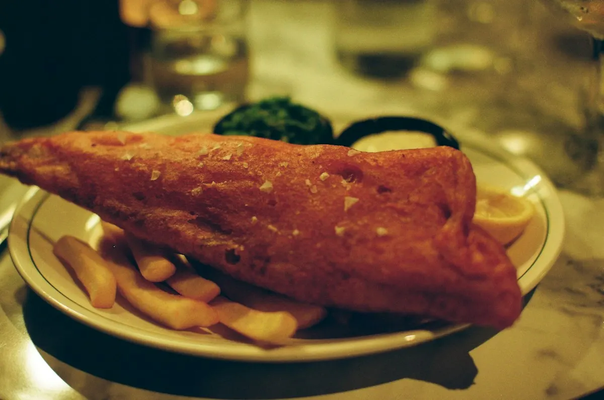 A large piece of battered fish with chips on a plate