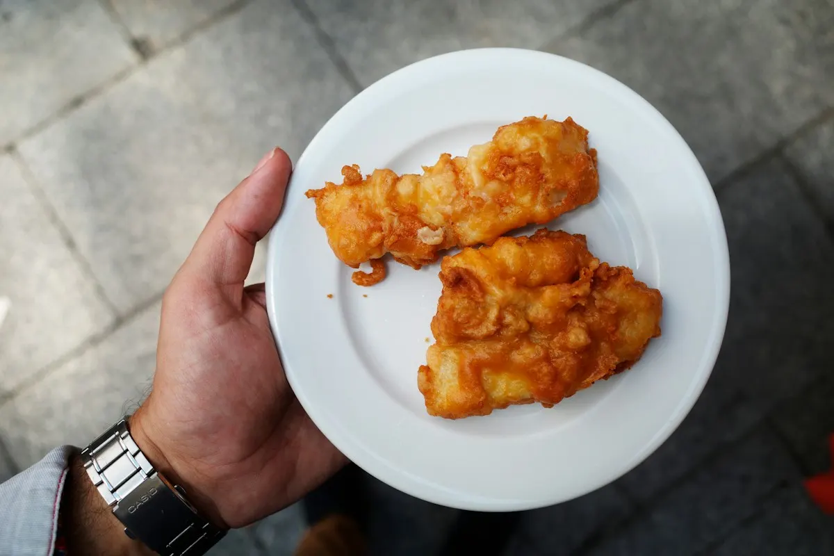 Golden fried fish on a plate held in one hand